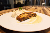 Salmon in Mustard Sauce Seared salmon in mustard sauce on a white plate with piped mashed potato and herb garnish