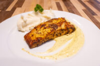 Salmon in Mustard Sauce Seared fillet of Salmon in Mustard Sauce beside mashed potatoes and a parsley sprig on a white plate.