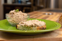 Sardines Dip or Spread Sardines Dip or Spread piled on toasted bread, with more in a glass bowl on a green plate.