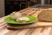 Sardines Dip or Spread Bowl of Sardines Dip or Spread beside a slice of bread topped with the spread, on a green plate with a loaf nearby.