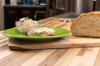 Sardines Dip or Spread Glass bowl of Sardines Dip or Spread beside a slice topped with it, with a crusty loaf on a wood board.