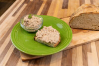 Sardines Dip or Spread Glass bowl of Sardines Dip or Spread beside a slice of bread topped with it, with a crusty loaf on a wooden board