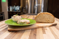 Sardines Dip or Spread Green plate with bowl of Sardines Dip or Spread and a topped bread slice, beside a whole loaf of bread on a wooden board