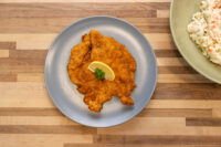 Golden breaded Chicken Schnitzel on a grey plate with lemon wedge and parsley garnish