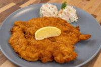 Golden fried Chicken Schnitzel topped with a lemon wedge, served on a gray plate with potato salad.