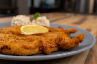 Golden breaded Chicken Schnitzel on a grey plate with a lemon wedge and creamy side salad.