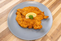 Golden breaded Chicken Schnitzel on a gray plate, garnished with a lemon slice and parsley.