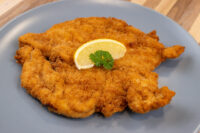 Golden fried Chicken Schnitzel on a grey plate, garnished with a lemon slice and parsley.