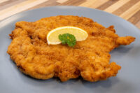 Golden-fried Chicken Schnitzel on a grey plate, garnished with a lemon wedge and parsley sprig.