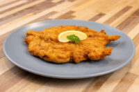 Golden fried Chicken Schnitzel on a grey plate with a lemon wedge and parsley, on a wooden table.