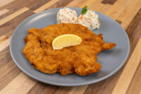 Golden fried Chicken Schnitzel on a grey plate with a lemon wedge and two scoops of creamy salad.