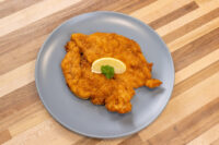 Golden fried Chicken Schnitzel on a grey plate with parsley and lemon wedge on wood table.