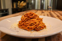 Spaghetti Bolognese Twirled mound of Spaghetti Bolognese on a white plate, topped with grated parmesan and pepper flecks.