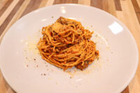 Spaghetti Bolognese Tall coil of Spaghetti Bolognese topped with grated parmesan and herbs on a white plate.