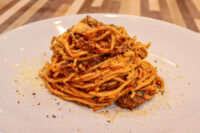 Spaghetti Bolognese Twirled spaghetti coated in bolognese meat sauce, topped with grated parmesan, on a white plate.