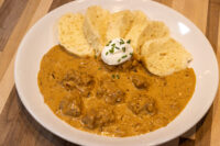 Bowl of Szegedin Goulash with creamy paprika sauce, sour cream, chives, and bread slices.
