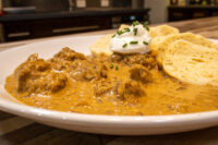 Bowl of Szegedin Goulash with tender meat in creamy paprika sauce, topped with sour cream and chives, bread on the side.