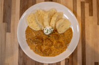 Bowl of Szegedin Goulash with creamy paprika sauce, sour cream garnish, and bread slices on a white plate.
