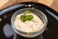 Glass bowl of Czech Tartar Sauce Tatarka topped with a fresh herb sprig, served on a black plate.