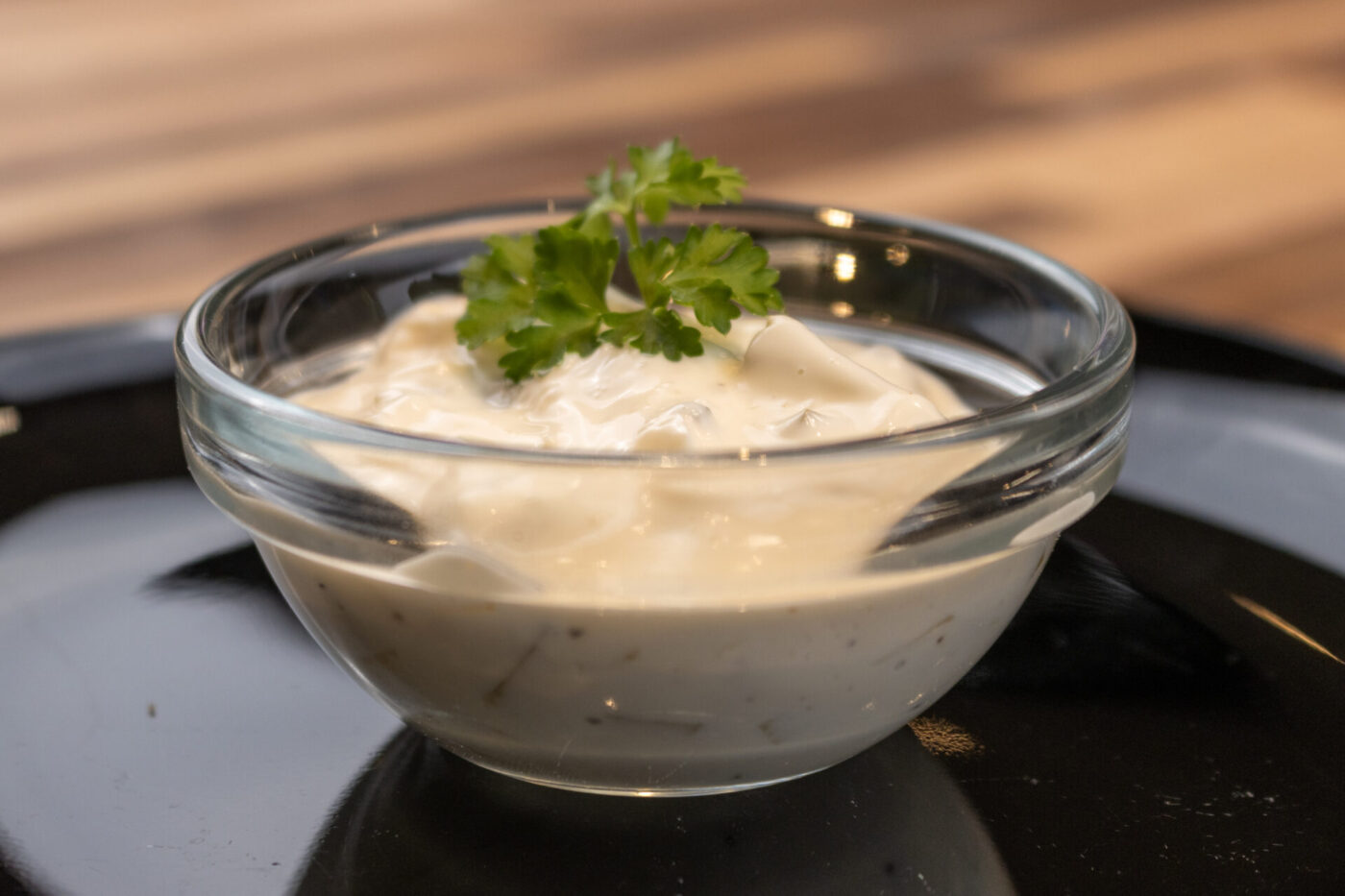 Glass bowl of Czech Tartar Sauce Tatarka garnished with a parsley sprig, set on a dark plate.