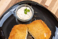 Jar of Czech Tartar Sauce Tatarka with parsley garnish beside a breaded fried cutlet on a black plate