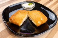 Breaded fried cutlet halves on a black plate, served with a small dish of Czech Tartar Sauce Tatarka.