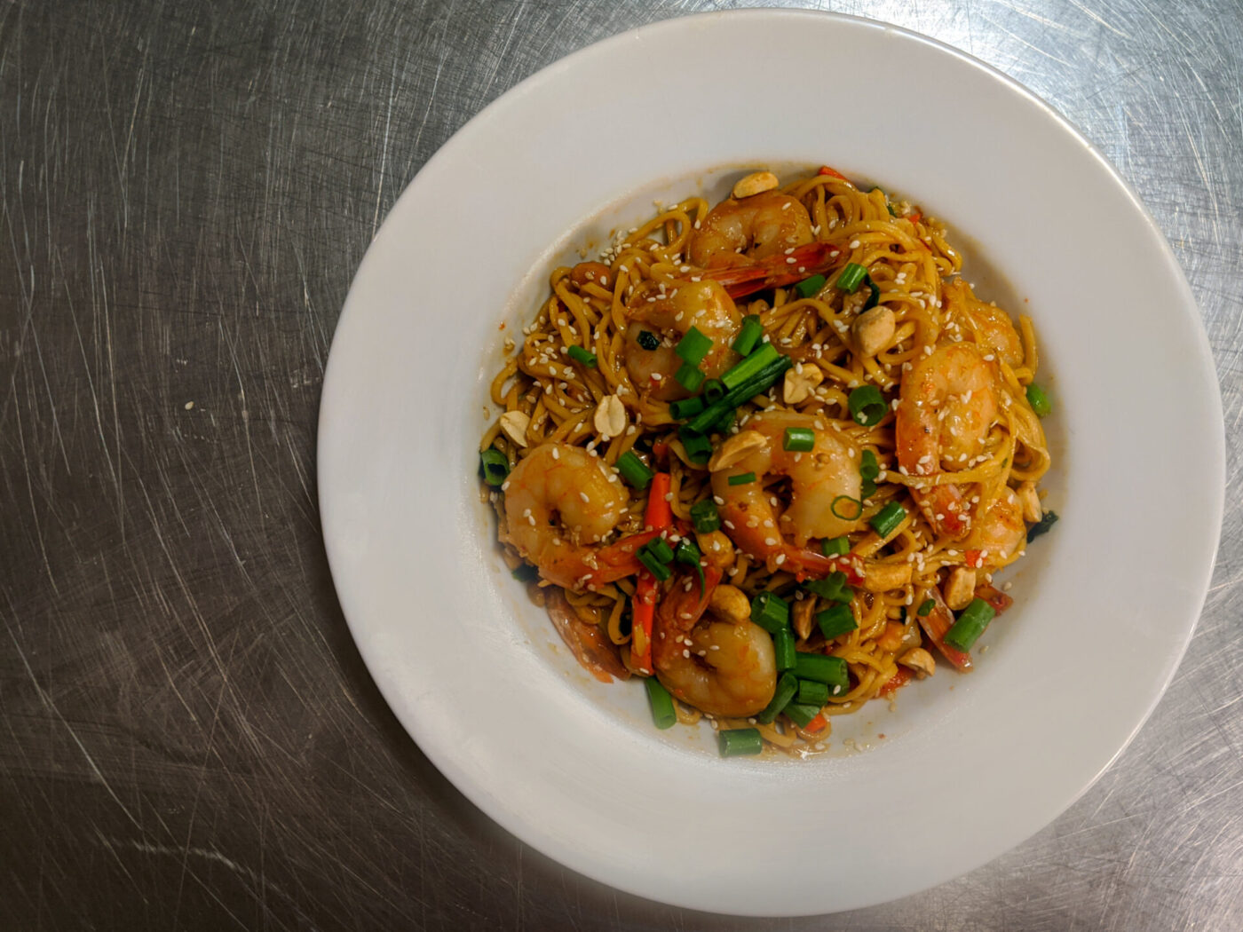 Thai Noodles with Shrimp Overhead shot of Thai Noodles with Shrimp topped with scallions, peanuts, and sesame seeds in a white bowl.