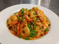 Thai Noodles with Shrimp White bowl of Thai Noodles with Shrimp topped with peanuts, green onions, and sesame seeds.