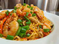 Thai Noodles with Shrimp Bowl of Thai Noodles with Shrimp topped with scallions, peanuts, and sesame seeds.
