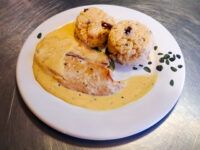 Tilapia in a Creamy Wine Sauce Sliced tilapia in creamy wine sauce on a white plate with two couscous rounds and herb garnish.