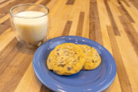 Chocolate Chip Cookies Two Chocolate Chip Cookies on a blue plate beside a glass of milk on a wood table