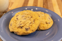 Chocolate Chip Cookies Two Chocolate Chip Cookies on a blue plate with a glass of milk behind them.