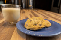 Chocolate Chip Cookies Two Chocolate Chip Cookies stacked on a blue plate next to a glass of milk on a wood table.