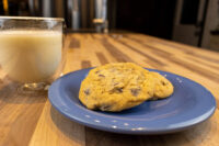 Chocolate Chip Cookies Two Chocolate Chip Cookies on a blue plate next to a glass mug of milk on a wood counter.
