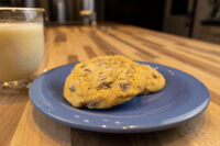 Chocolate Chip Cookies A Chocolate Chip Cookies cookie on a blue plate with a glass of milk on a wooden counter