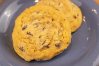 Chocolate Chip Cookies Two golden Chocolate Chip Cookies with cracked tops rest on a gray plate.
