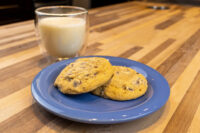Chocolate Chip Cookies Two Chocolate Chip Cookies on a blue plate beside a glass of milk on a wood table.