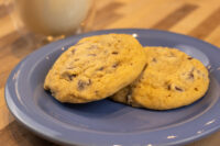 Chocolate Chip Cookies Two Chocolate Chip Cookies stacked on a blue plate with a glass of milk blurred behind them.