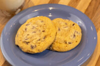 Chocolate Chip Cookies Two golden Chocolate Chip Cookies on a blue plate with a glass of milk behind them.