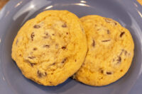 Chocolate Chip Cookies Two golden Chocolate Chip Cookies with visible chocolate chunks resting on a blue plate.