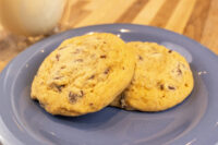 Chocolate Chip Cookies Two Chocolate Chip Cookies stacked on a blue plate with a glass of milk behind them.