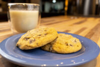 Chocolate Chip Cookies Two Chocolate Chip Cookies stacked on a blue plate beside a glass of milk on a wooden table.