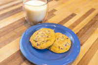 Chocolate Chip Cookies Two Chocolate Chip Cookies on a blue plate with a glass of milk behind them on a wood table