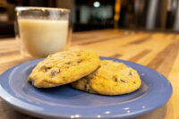Chocolate Chip Cookies Two Chocolate Chip Cookies stacked on a blue plate with a glass of milk on a wooden table.