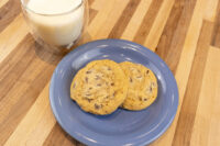 Chocolate Chip Cookies Two Chocolate Chip Cookies on a blue plate with a glass of milk on a wood table