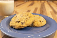 Chocolate Chip Cookies Two Chocolate Chip Cookies on a blue plate beside a glass of milk on a wooden table