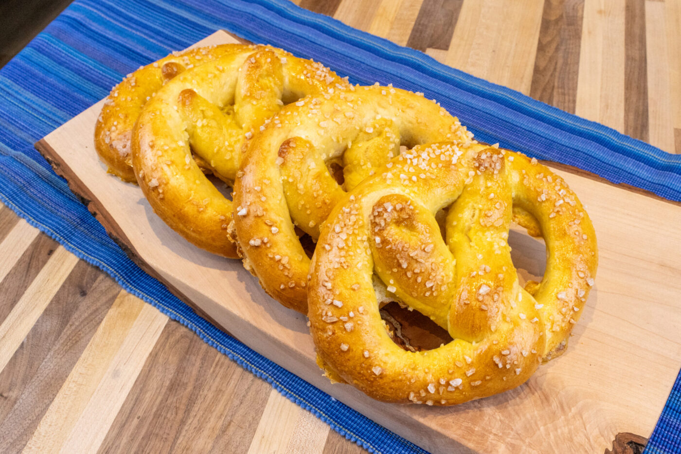 Czech Soft Pretzel Preclík Recipe Three golden Czech Soft Pretzel Preclík topped with coarse salt on a wooden board with blue striped cloth