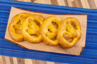 Czech Soft Pretzel Preclík Recipe Four golden Czech Soft Pretzel Preclík with coarse salt on a wooden board over blue striped cloth