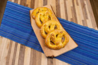Czech Soft Pretzel Preclík Recipe Three golden Czech Soft Pretzel Preclík with coarse salt on a wooden board over a blue striped runner.