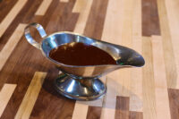 Filet Mignon with Demi-Glace Sauce Silver gravy boat filled with dark brown Demi-Glace Sauce on a striped wooden surface.